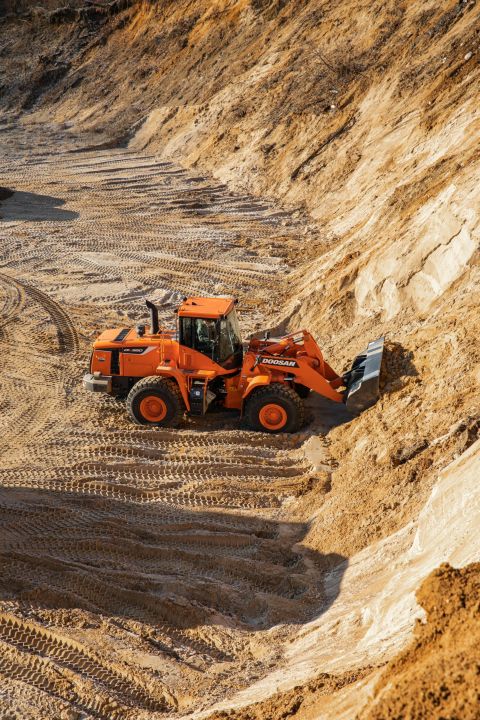 Orange wheel loader working in a sandy excavation site with tire tracks and a steep dirt slope in the background.